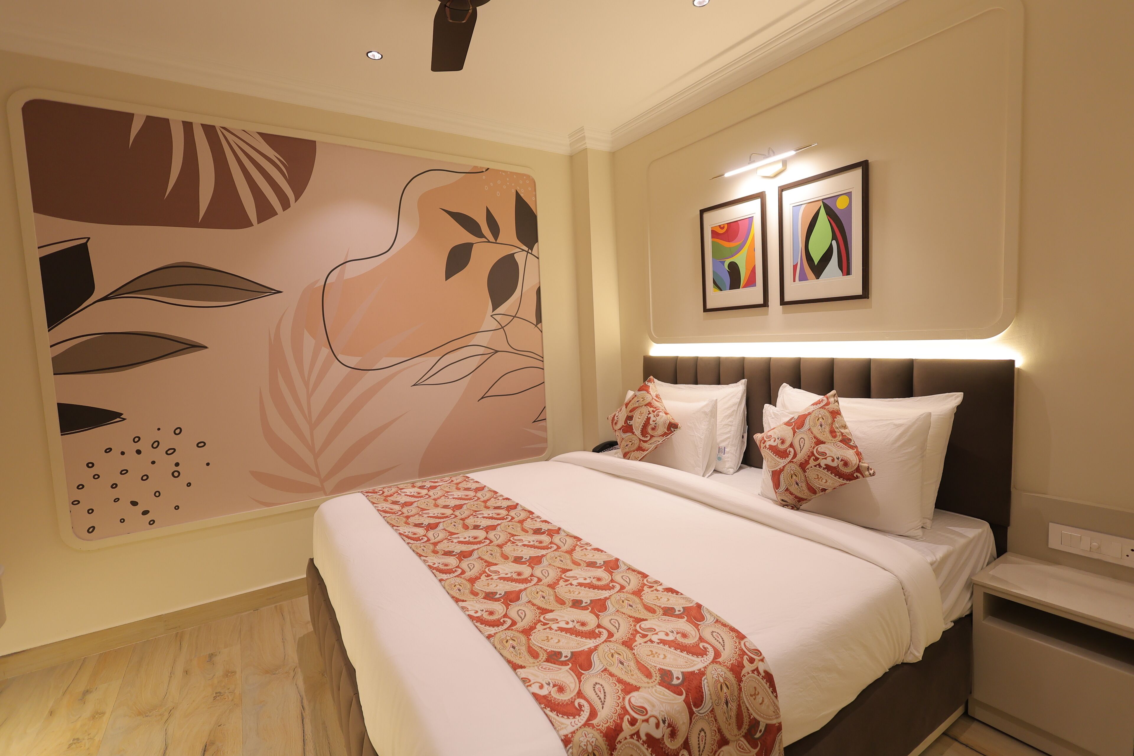 Una habitación de hotel con una cama grande, una mesita de noche, una pared decorada con arte abstracto y un ventilador de techo.