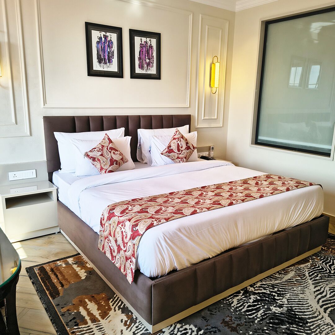 A neatly made bed with a patterned bedspread, a brown upholstered headboard, and two framed artworks on the wall.