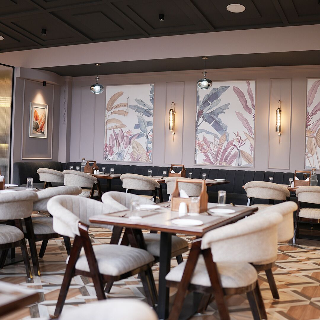 A restaurant with high-backed chairs, a patterned floor, and wall-mounted light fixtures.