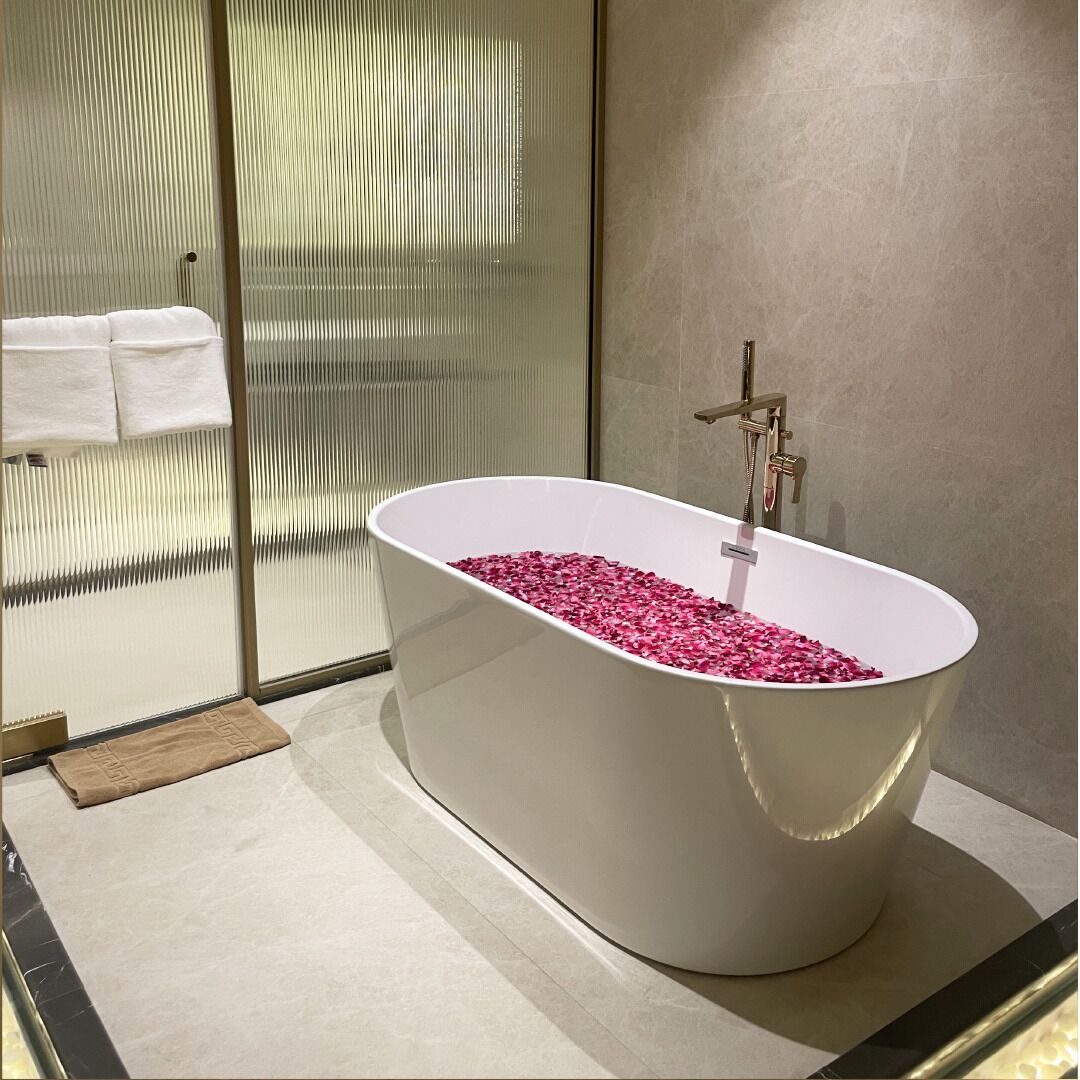 A modern bathroom with a freestanding bathtub filled with rose petals, a glass shower enclosure, and a towel rack with white towels.