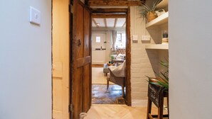 A wooden door leading into a room with a white brick wall, a small table with a plant, and a sign that reads "Mouh by Claire." - Two Cottages near Stratford-upon-Avon (Clifford Chambers)