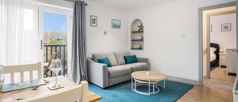 A modern living room with a grey sofa, a wooden coffee table, and a dining area with a table and chairs.