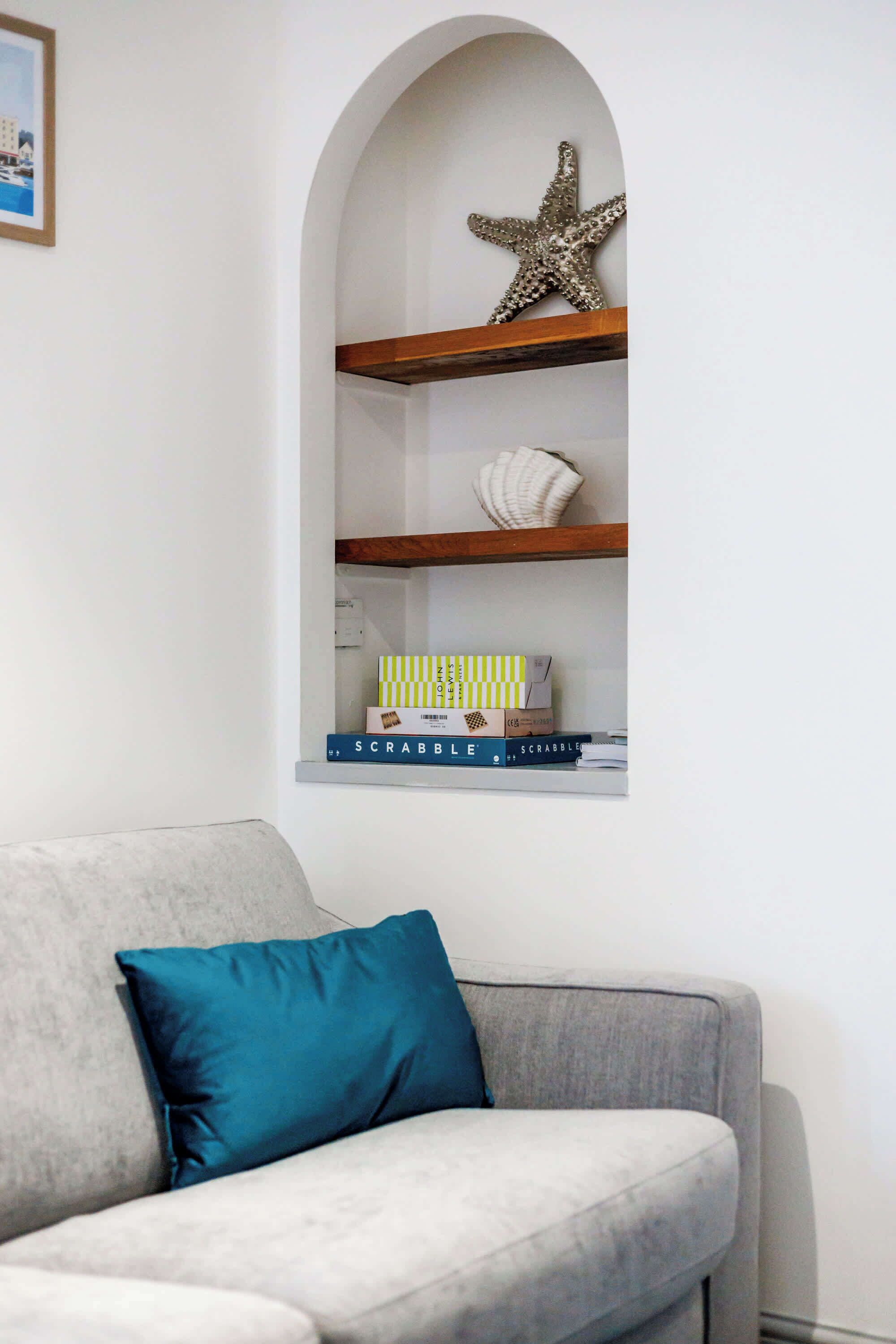 Uma sala de estar com um sofá cinza, uma almofada verde-água e uma estante com livros e objetos decorativos.