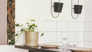 Een moderne keuken met een zwart aanrecht, twee bruine leren stoelen, een potplant, een wijnglas en twee zwarte wandlampen.