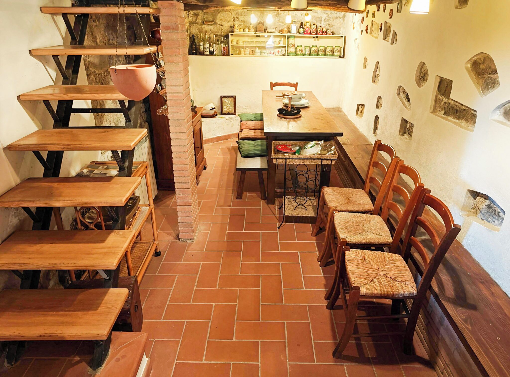 Un comedor rústico con bancos y sillas de madera, suelo de baldosas y pared de ladrillo.