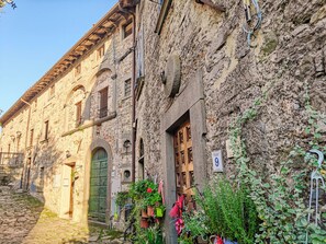A stone building with arched doorways and windows, a cobblestone street, and potted plants outside. - Casa Rosa (Pescaglia)