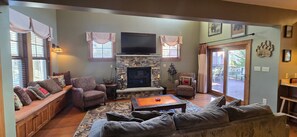A cozy living room with a stone fireplace, comfortable seating, and a television mounted above it. - Better At The Lake | 4BR/3BA Oakland | Hot Tub (Oakland)