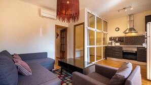 A modern apartment with a living room featuring a gray sofa and a coffee table, a kitchen with dark cabinets and a stainless steel range hood, and a large window with a view of the interior. - Ramon Turró - Nice apartment in Poble Nou near the beach (Barcelona)