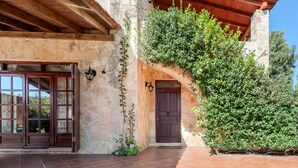 A stone building with a wooden door and windows, a tiled patio, and a green hedge. - Skine Dream Villa, Charming Villa with Private Pool (Platanias)