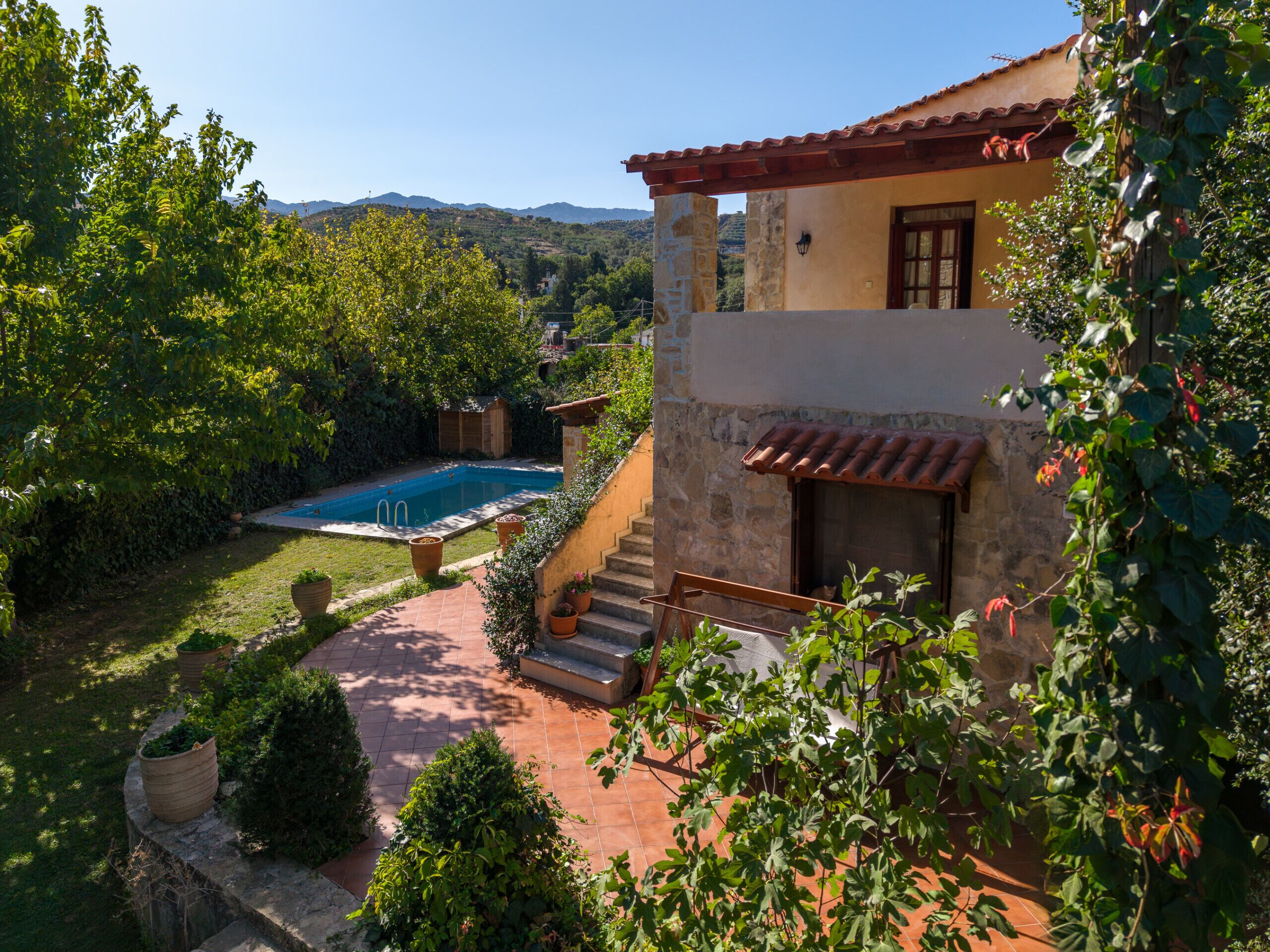 A two-story house with a swimming pool, surrounded by lush greenery and hills in the background.