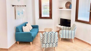 Een woonkamer met een blauwe bank, gestreepten fauteuils, een klein rond tafeltje en een televisie.
