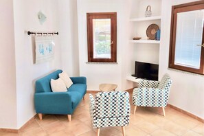 A living room with a blue sofa, patterned armchairs, a small round table, and a TV. - Rosemary Villa 6 beds (Muravera)