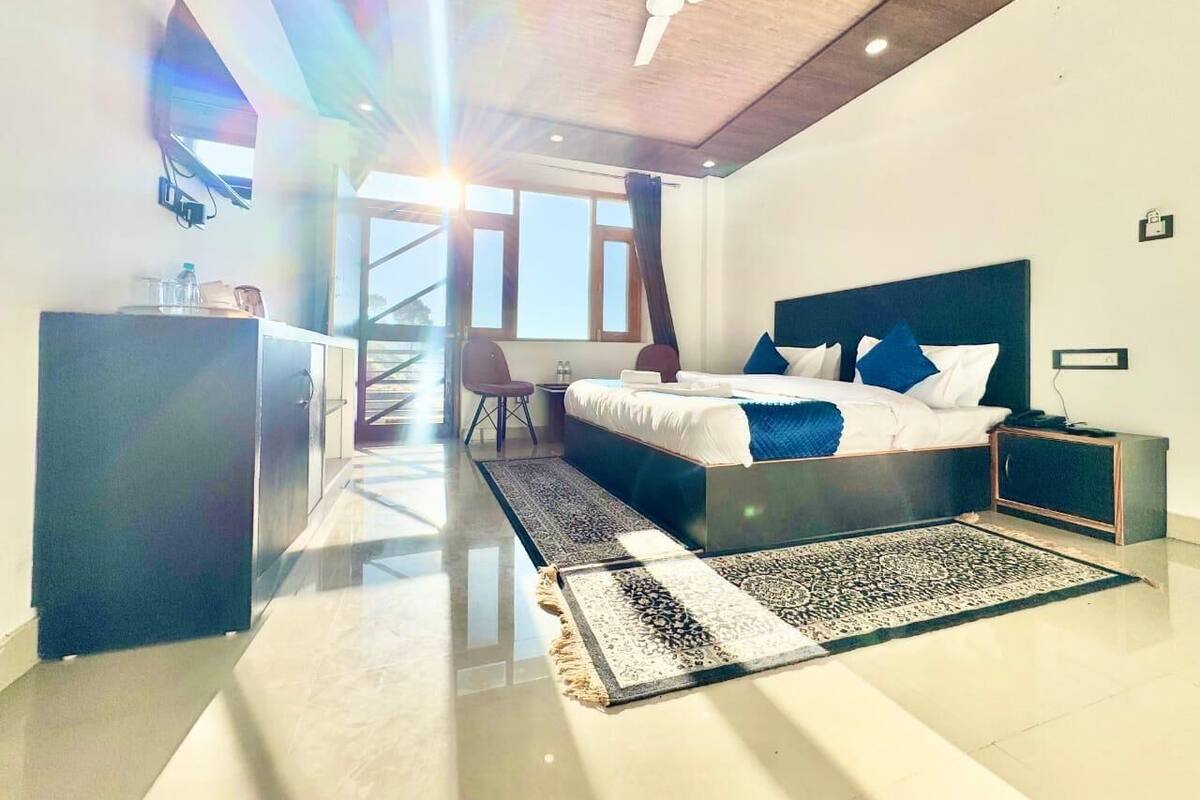 Une chambre moderne avec un grand lit, un bureau et une chaise. On y trouve un ventilateur de plafond et une fenêtre avec des rideaux.