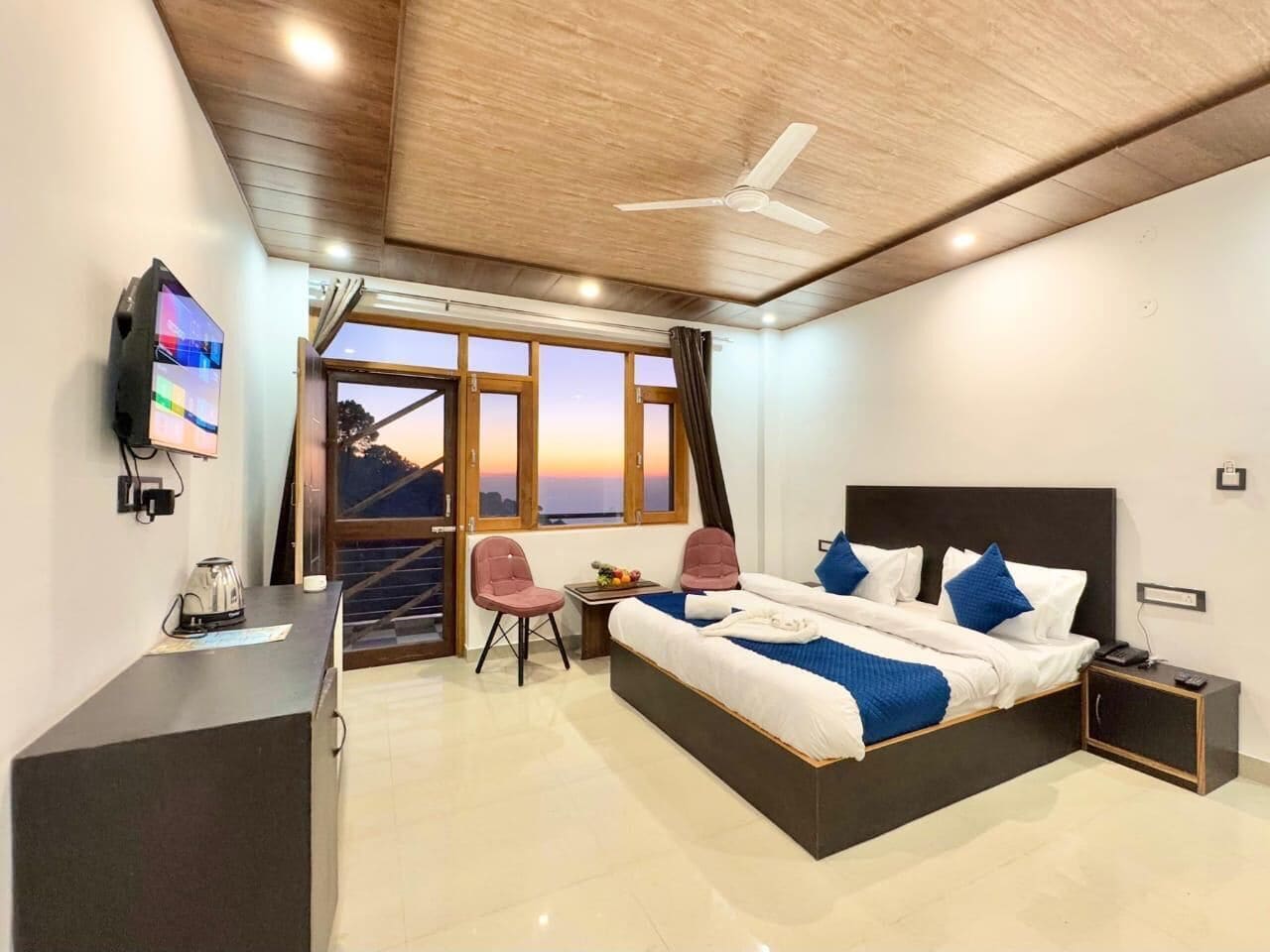 Une chambre d’hôtel moderne dotée d’un grand lit, d’un bureau avec une bouilloire, d’une télévision et offrant une vue sur le coucher du soleil à travers les fenêtres.