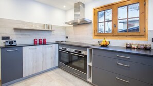 Une cuisine moderne équipée d’un four encastré, d’un four à micro-ondes et d’une cuisinière. Une fenêtre aux cadres en bois offre une vue sur un paysage enneigé.