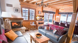 Un salon chaleureux avec une cheminée, des fauteuils confortables et de grandes fenêtres.