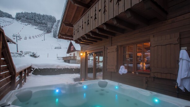 Une construction en bois dotée d’un bain à remous et offrant une vue sur une montagne enneigée.
