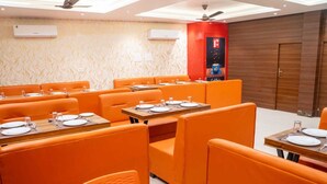 Un restaurant avec des banquettes et des tables orange, des climatiseurs fixés aux murs et un ventilateur au plafond.