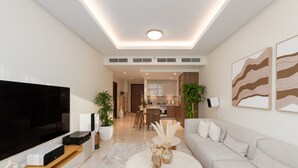 Een moderne woonkamer met een flatscreen-televisie, een bijzettafeltje met decoratieve objecten, een bank en een keuken op de achtergrond.