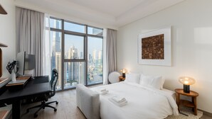 Een moderne hotelkamer met een groot raam met uitzicht op de stad, een opgemaakt bed, een bureau met een computer en een stoel.