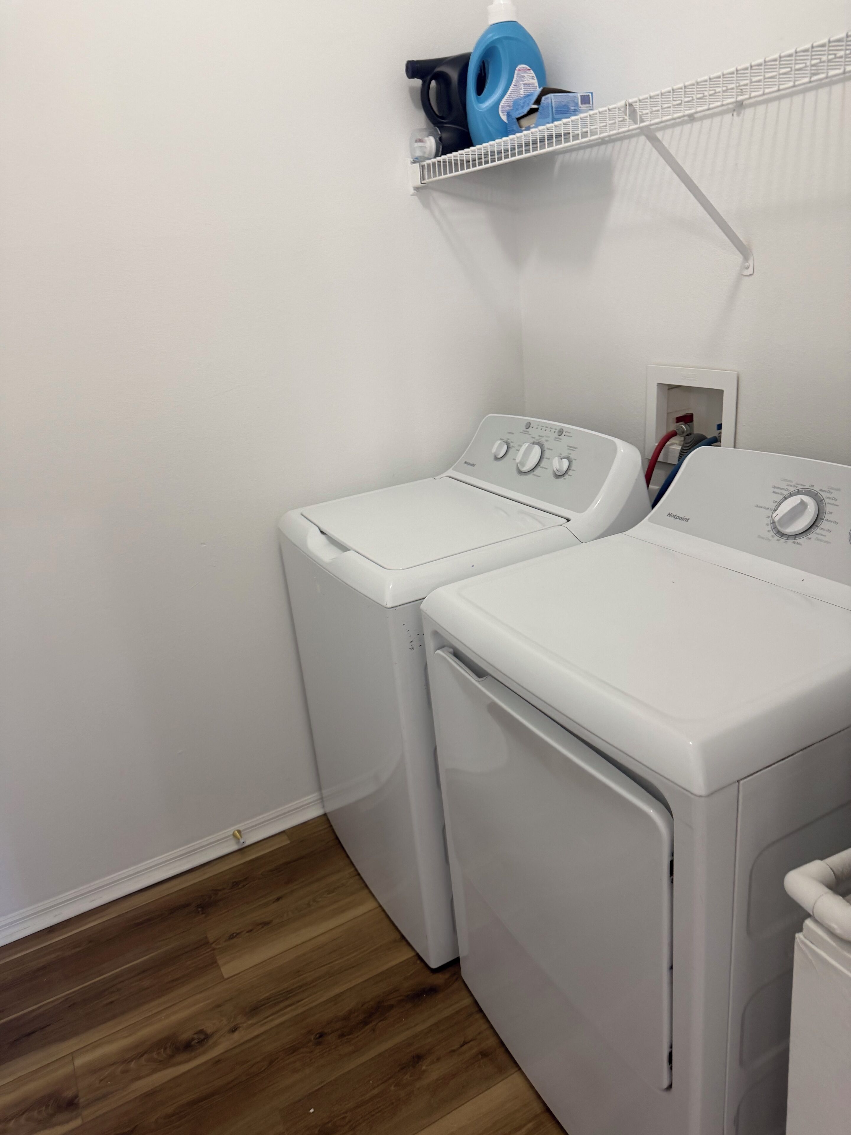 Un área de lavandería con dos lavadoras blancas, un estante con productos de limpieza y suelo de madera.