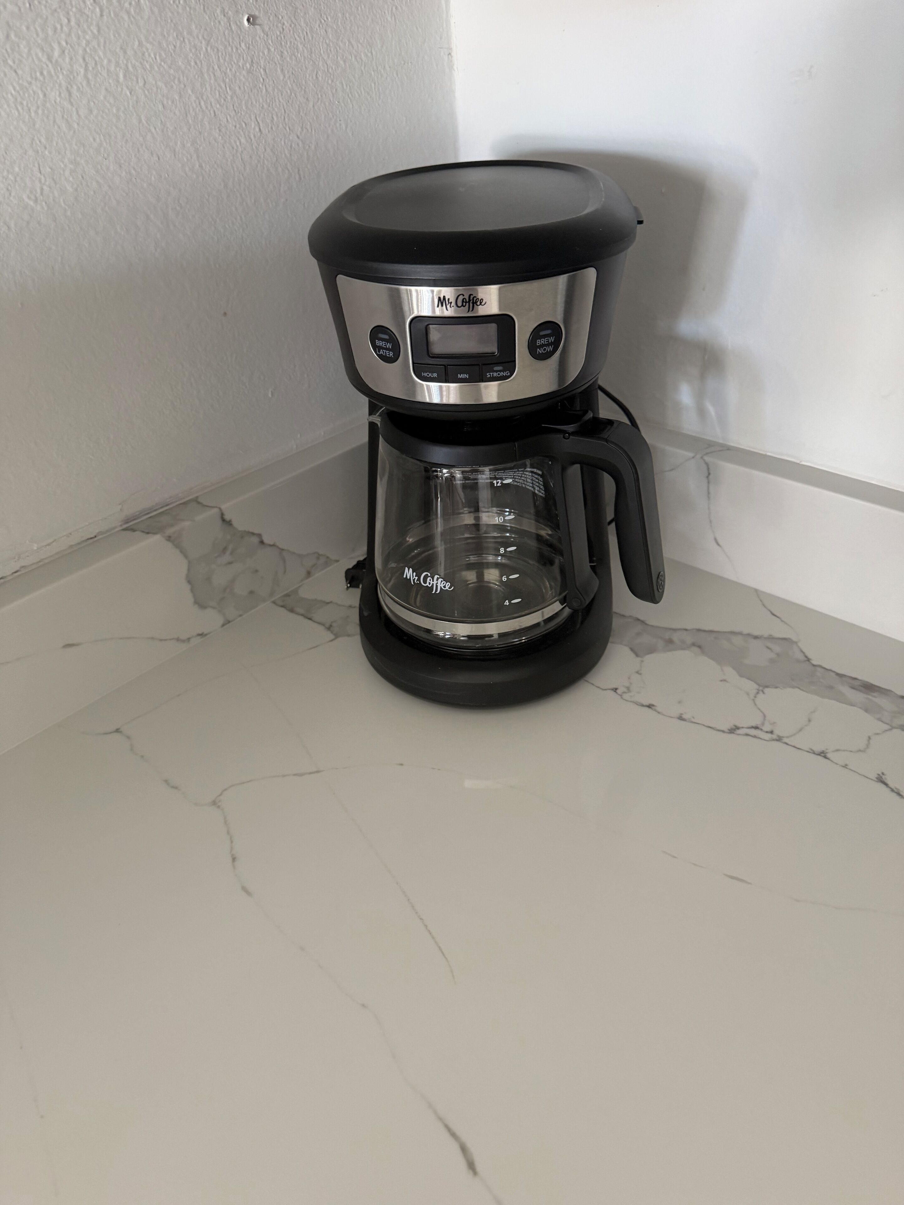 Une machine à café dotée d’un écran numérique et d’une verseuse en verre, posée sur un comptoir en marbre.