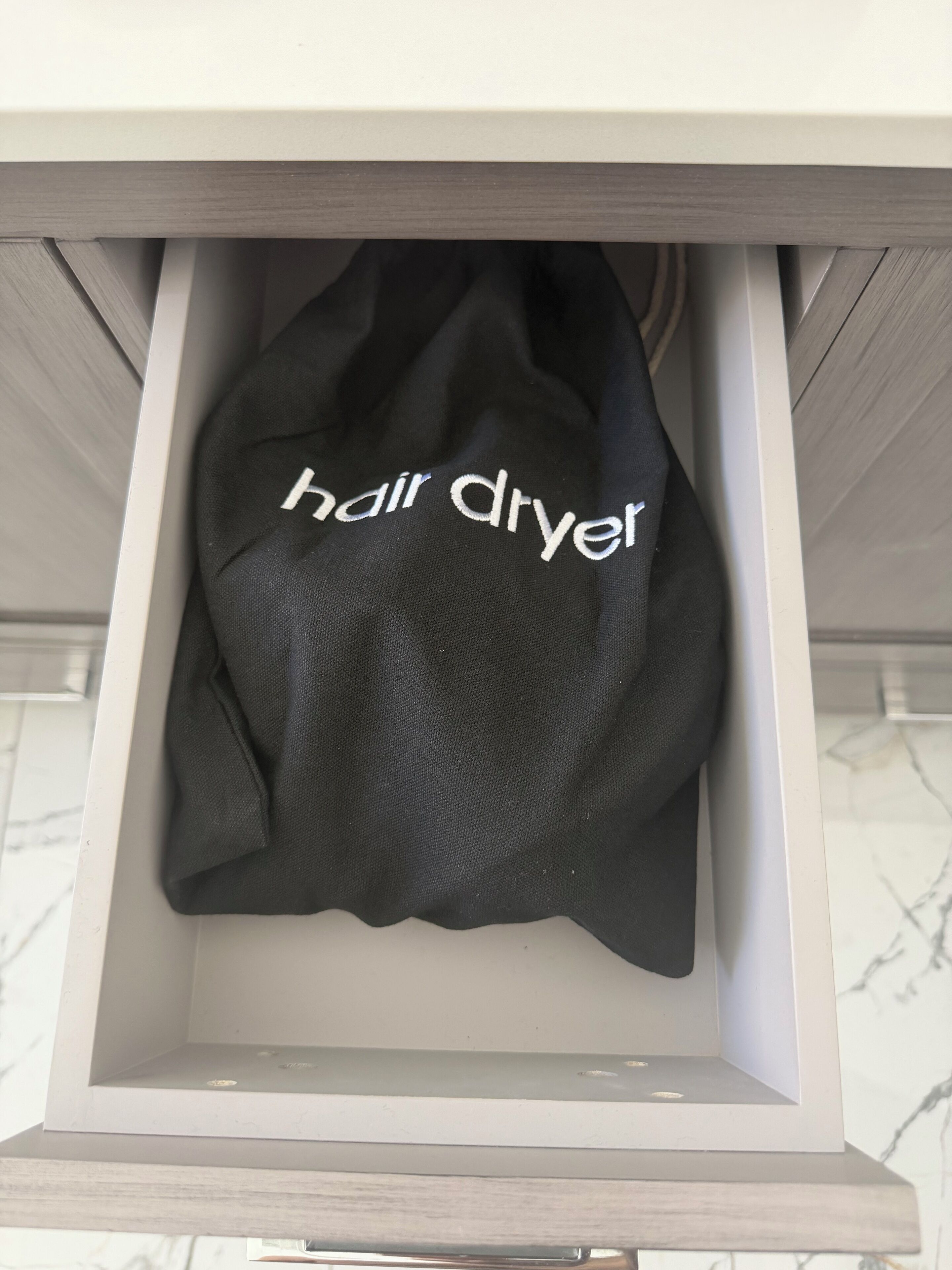 A drawer containing a black bag with the text "hair dryer" on it.