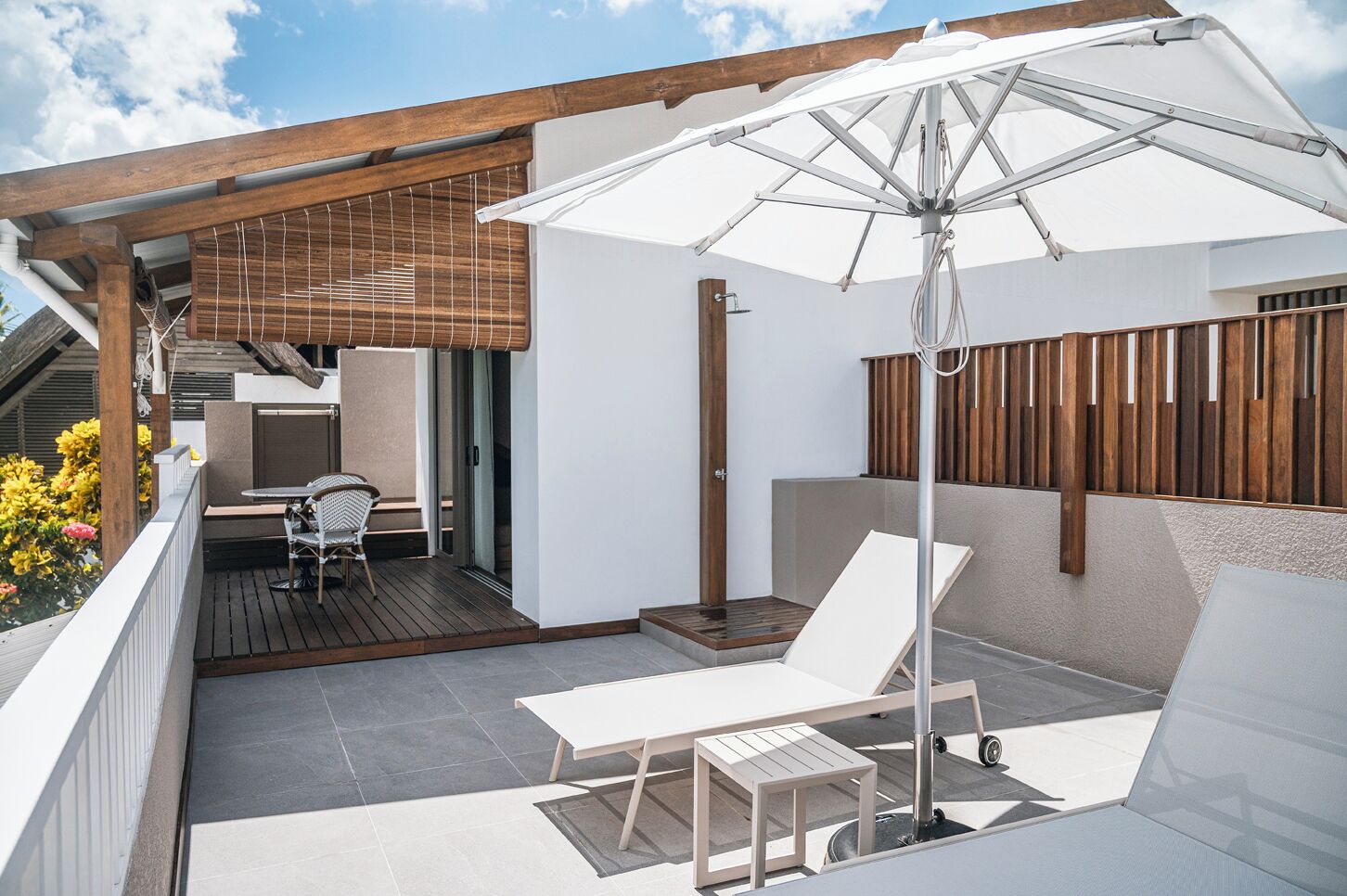 Une terrasse avec une table et des chaises, un parasol blanc et une clôture en bois.
