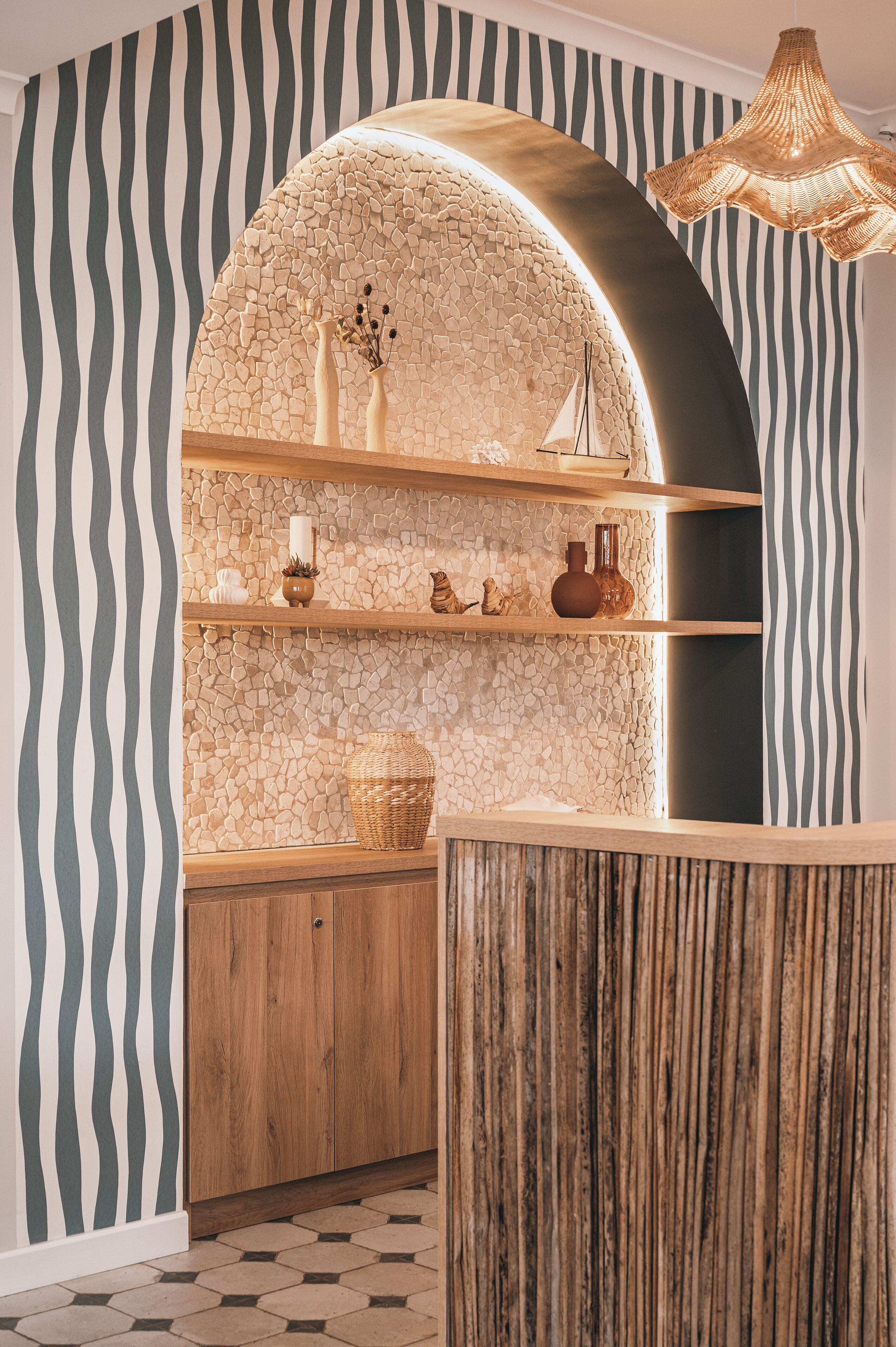 Un área de recepción con una pared curva, estanterías de madera y una lámpara de fibra trenzada.