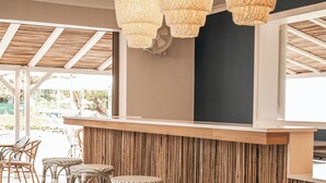Zona de bar con taburetes de mimbre, una barra de madera y un techo con lámparas de entramado.