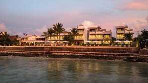 Un hotel frente a la playa con varias edificaciones, zonas de estar al aire libre y vista al mar.