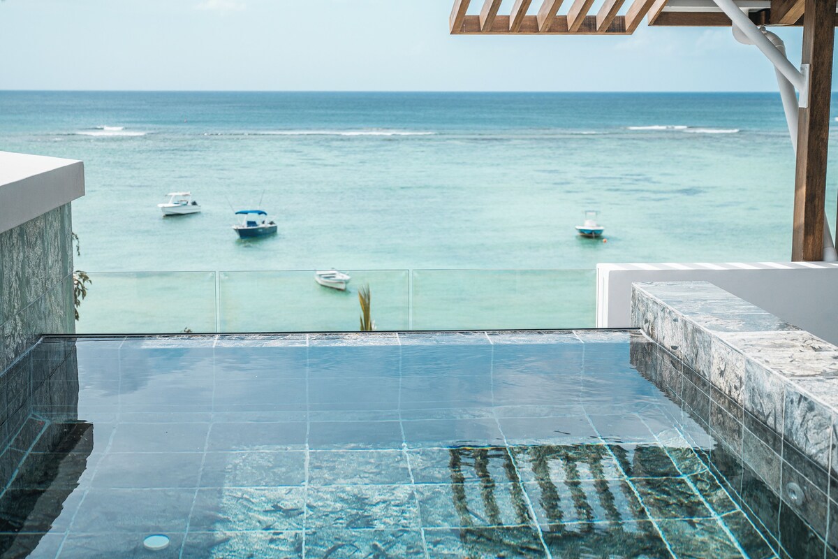 A clear view of a swimming pool with a glass barrier, overlooking the sea with several boats.