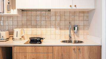 Une cuisine moderne avec des meubles blancs, un pare-feu en carrelage, un évier en acier inoxydable, une bouilloire, un grille-pain et des meubles bas en bois.