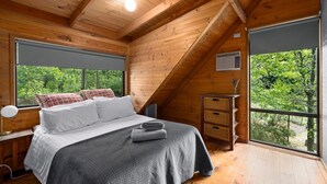 Quarto de cabana de madeira com cama, mesa de cabeceira, janela e vista para o verde.