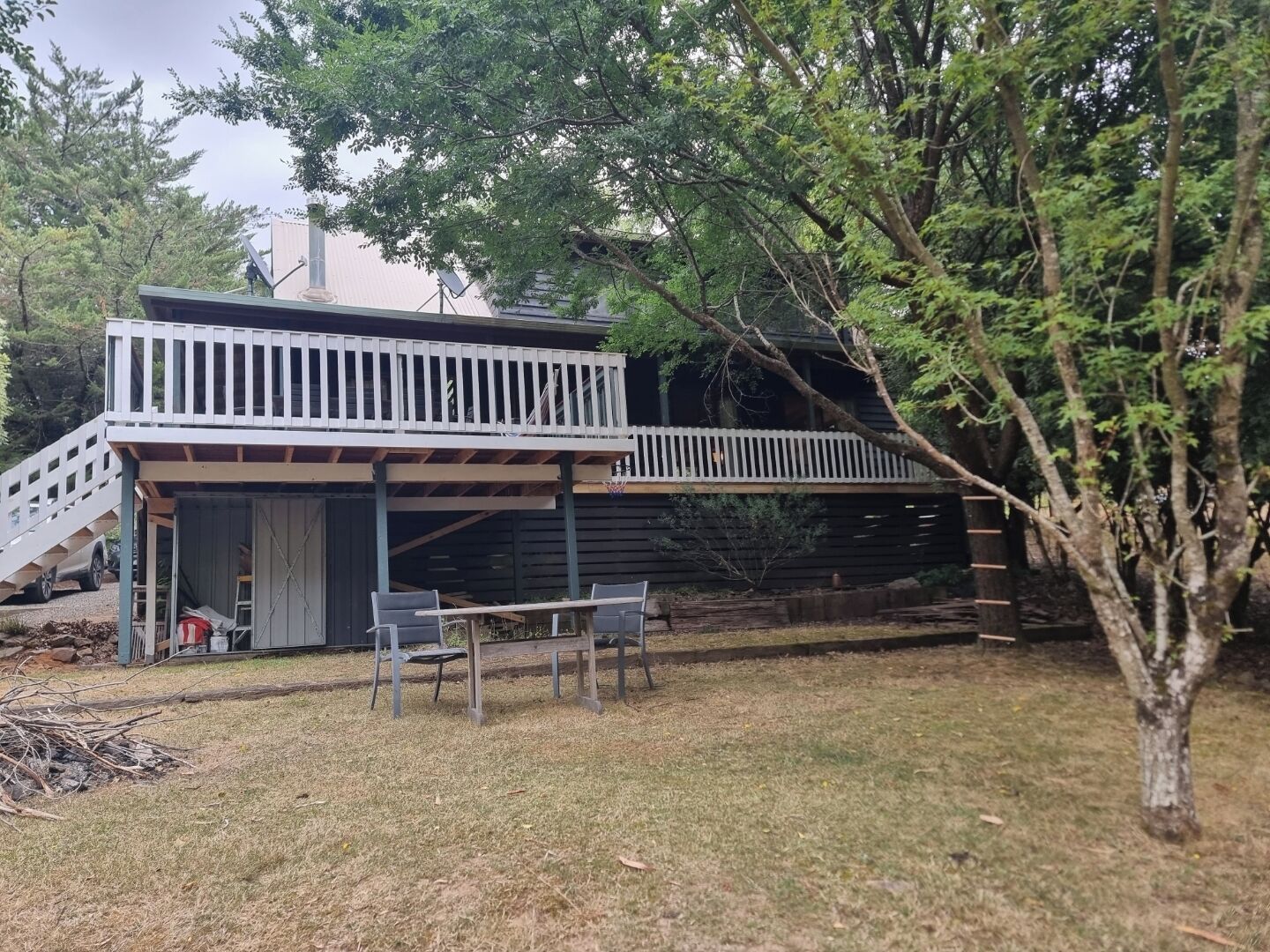A two-story wooden house with a balcony, a covered patio area, and a small outdoor seating space.