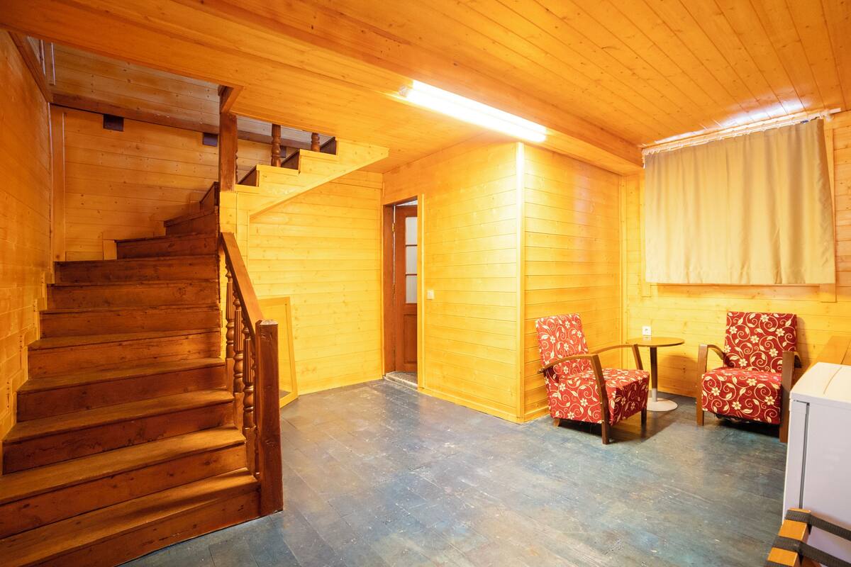 A wooden interior with a staircase, two chairs, a table, and a kettle.