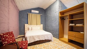 A bedroom with a bed, a wooden wardrobe, a chair, and a patterned cushion. - Welt bungslows  (Konyaalti)