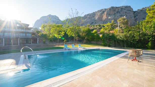 A swimming pool with a clear blue water, surrounded by a tiled deck, and a mountain in the background. - Welt bungslows  (Konyaalti)