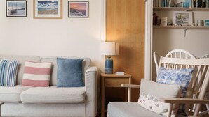 Een woonkamer met een bank, een stoel, een bijzettafeltje met een lamp en een boekenkast.