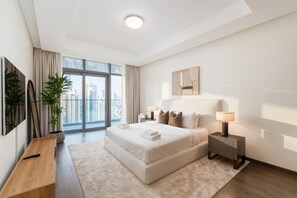 Quarto moderno com uma cama grande, mesas de cabeceira, uma planta em vaso e vista da cidade através de janelas amplas.