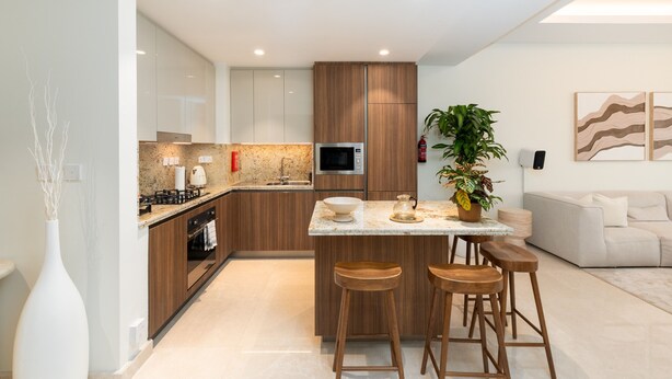 A modern kitchen with a central island, wooden cabinets, and a microwave. - Prime 2BR Downtown Iconic Burj View (Dubai)