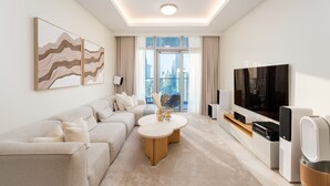 A modern living room with a sofa, a coffee table, a TV, and a city view through large windows. - Prime 2BR Downtown Iconic Burj View (Dubai)