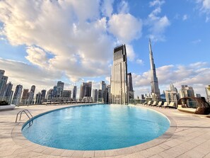 Uma piscina com um horizonte urbano ao fundo, incluindo edifícios altos e céu claro.