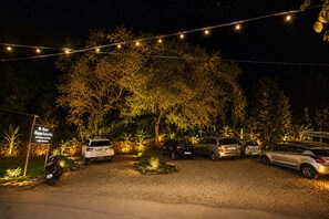 A hotel entrance at night with string lights, parked cars, and a sign indicating 'Hotel Happy Forest Inn.'