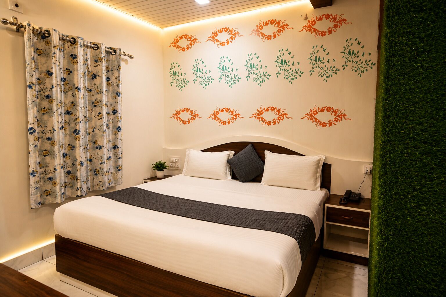 A neatly made bed with a headboard, a bedside table with a lamp, and a wall with floral wall decals.