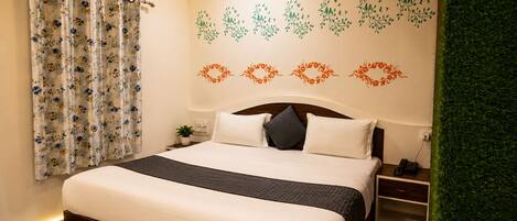 A neatly made bed with a headboard, a bedside table with a lamp, and a wall with floral wall decals.