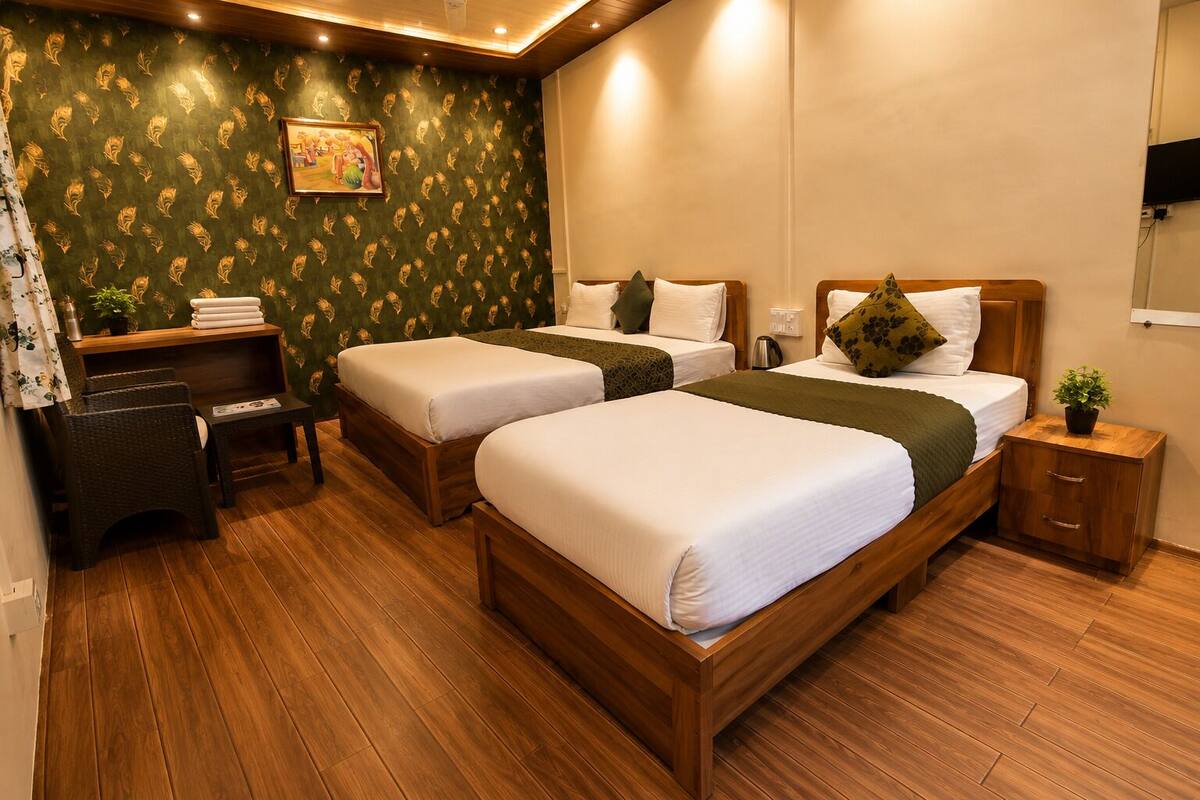 A hotel room with two single beds, a wooden nightstand, a small table, a bench, a wall-mounted TV, and a patterned wallpaper.