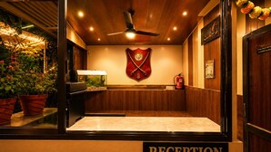 A reception area with a wooden ceiling, a ceiling fan, a fire extinguisher, and a wall-mounted emblem. - Hotel Happy Forest - Boutique Garden Retreat in Mount Abu (Mount Abu)