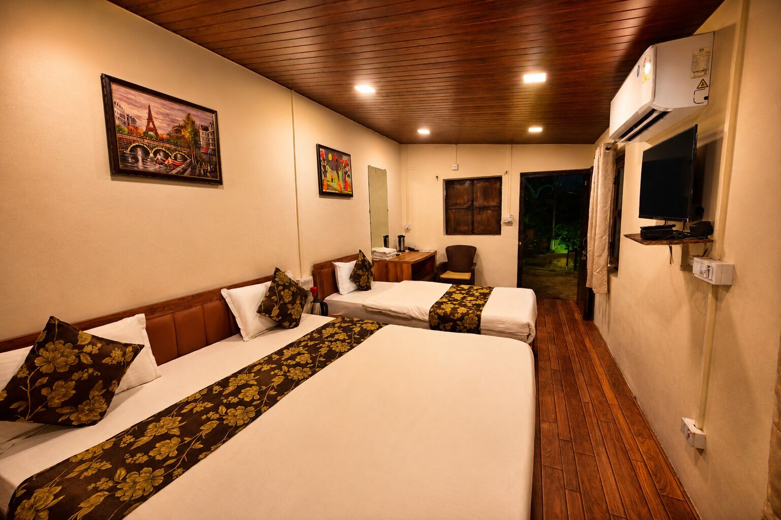 A hotel room with two beds, a desk, a chair, a TV, and a painting of a bridge.