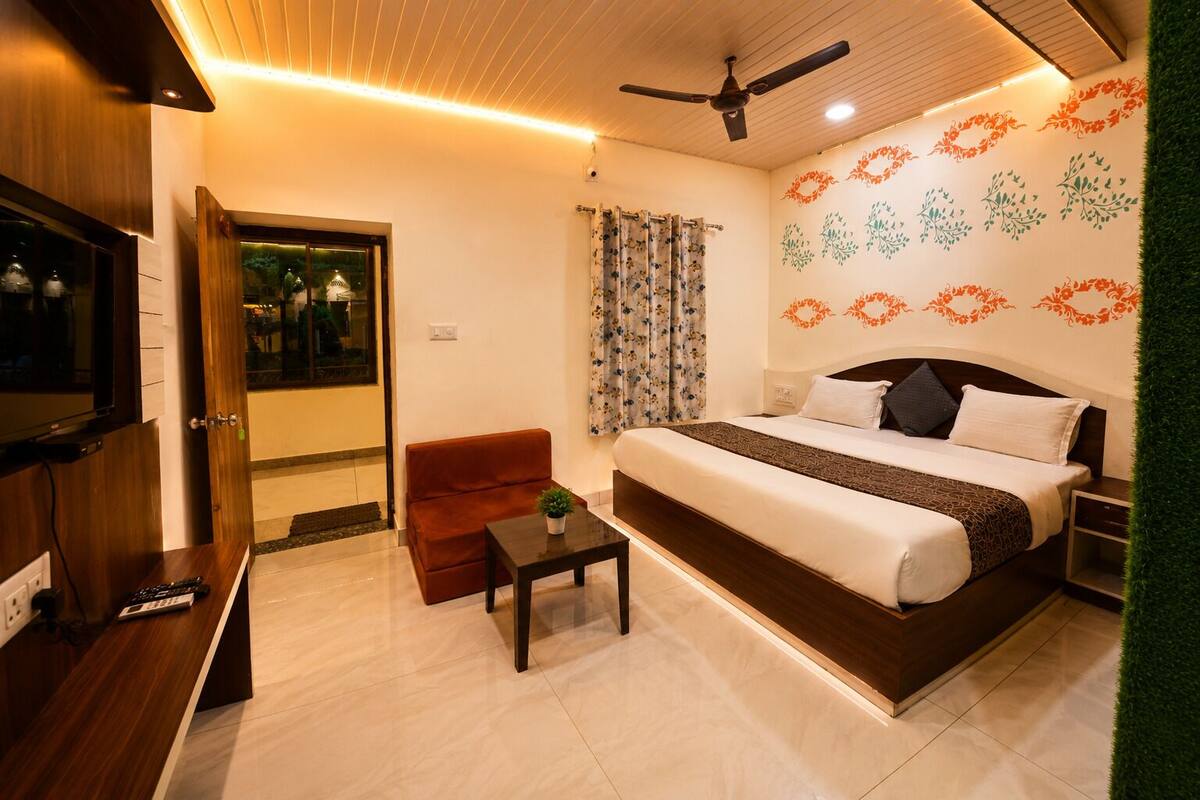 A hotel room with a bed, a TV, a sofa, a small table, and a ceiling fan.